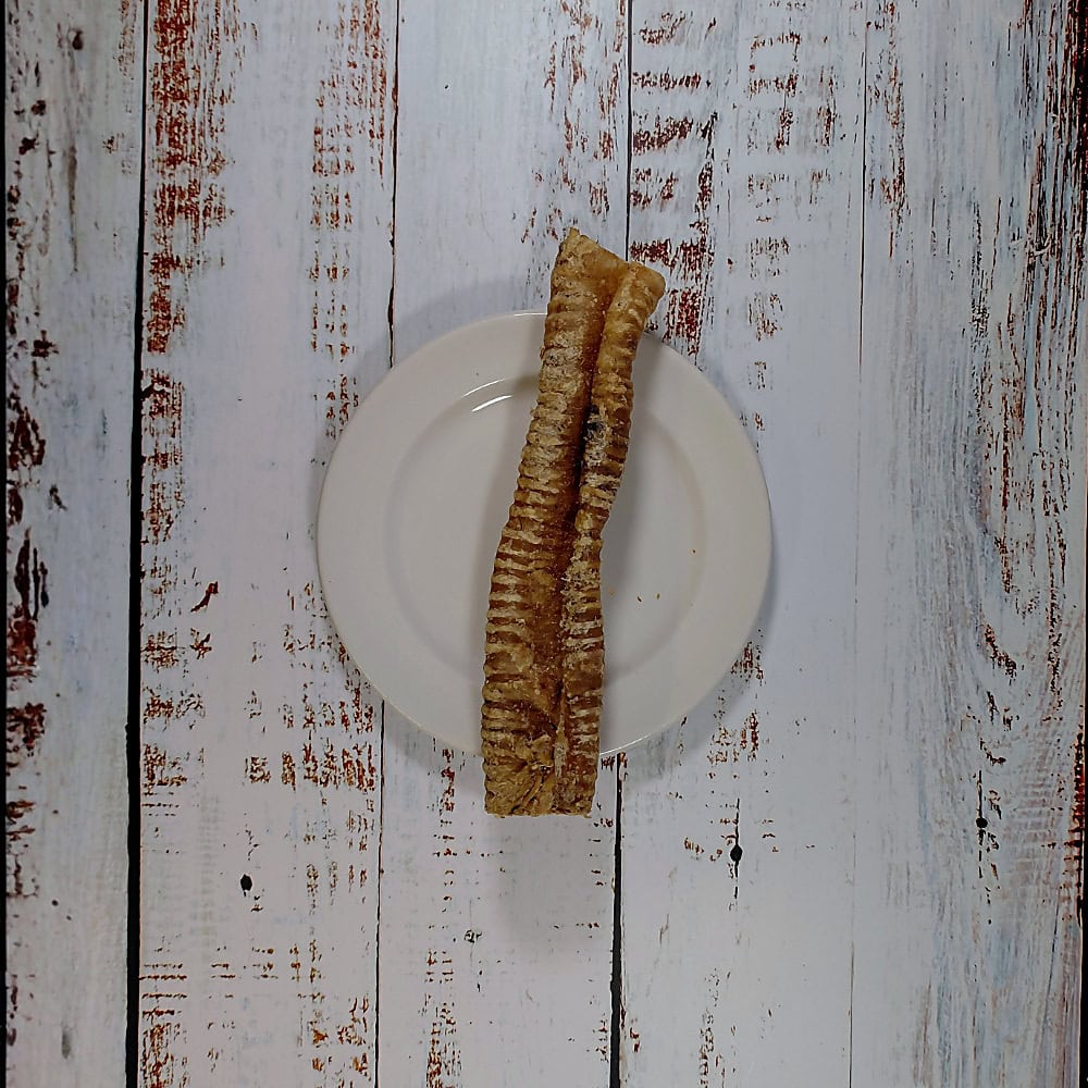 A hand holding two Buffalo Tubes dog chews above a cream plate to show their length