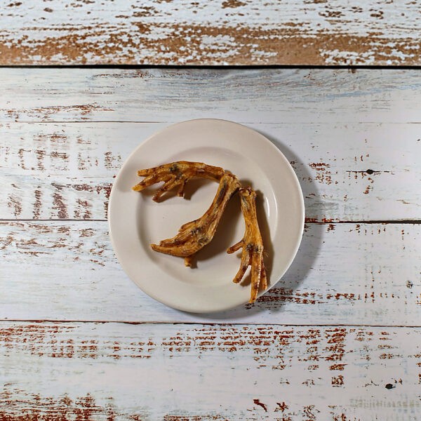 Three dried chicken feet dog chews on a cream plate on a whitewashed wooden board