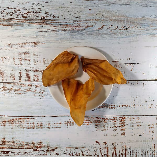 Three Cows Ears natural dog chews on a cream plate on a whitewashed wooden board