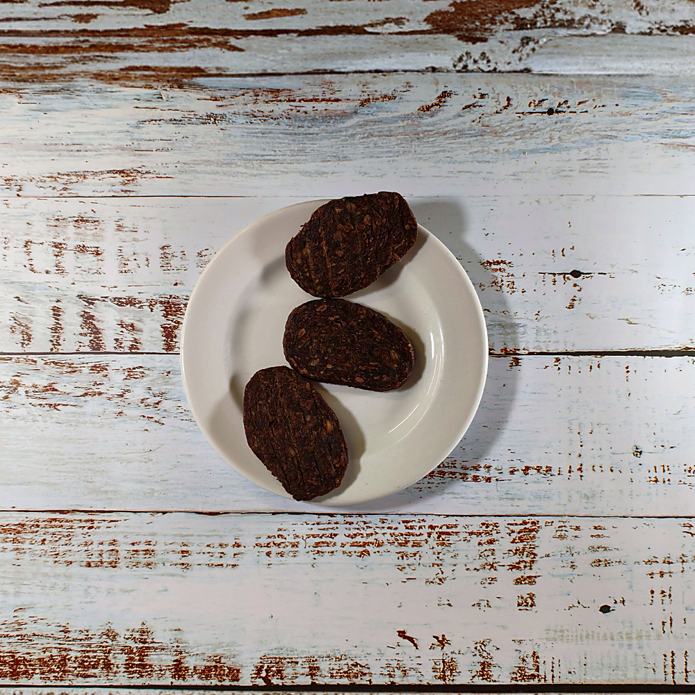 Three duck and chicken grills dog treats on a cream plate on a whitewashed wooden board