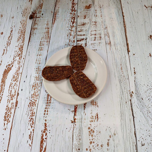 Three duck and chicken grills dog treats on a cream plate on a whitewashed wooden board