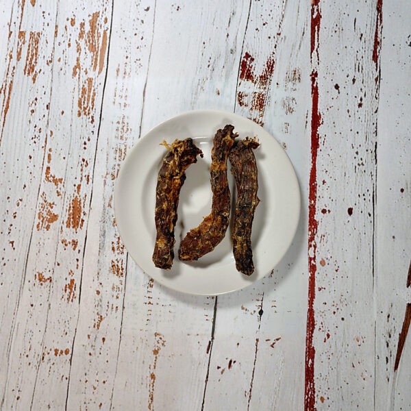 Three duck necks natural dog chews on a cream plate on a whitewashed wooden board