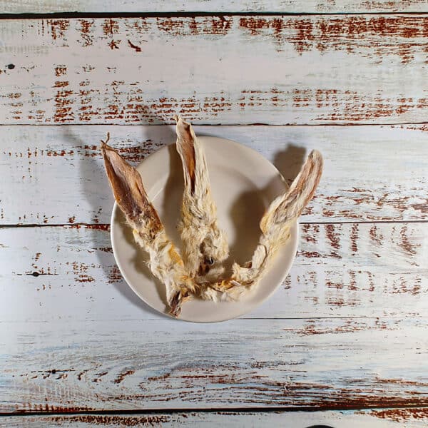 Three hairy rabbit ears dog chews on a cream plate on a whitewashed wooden board