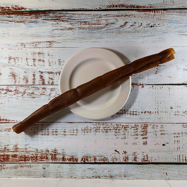 A large camel roll dog chew on a cream plate on a whitewashed wooden board
