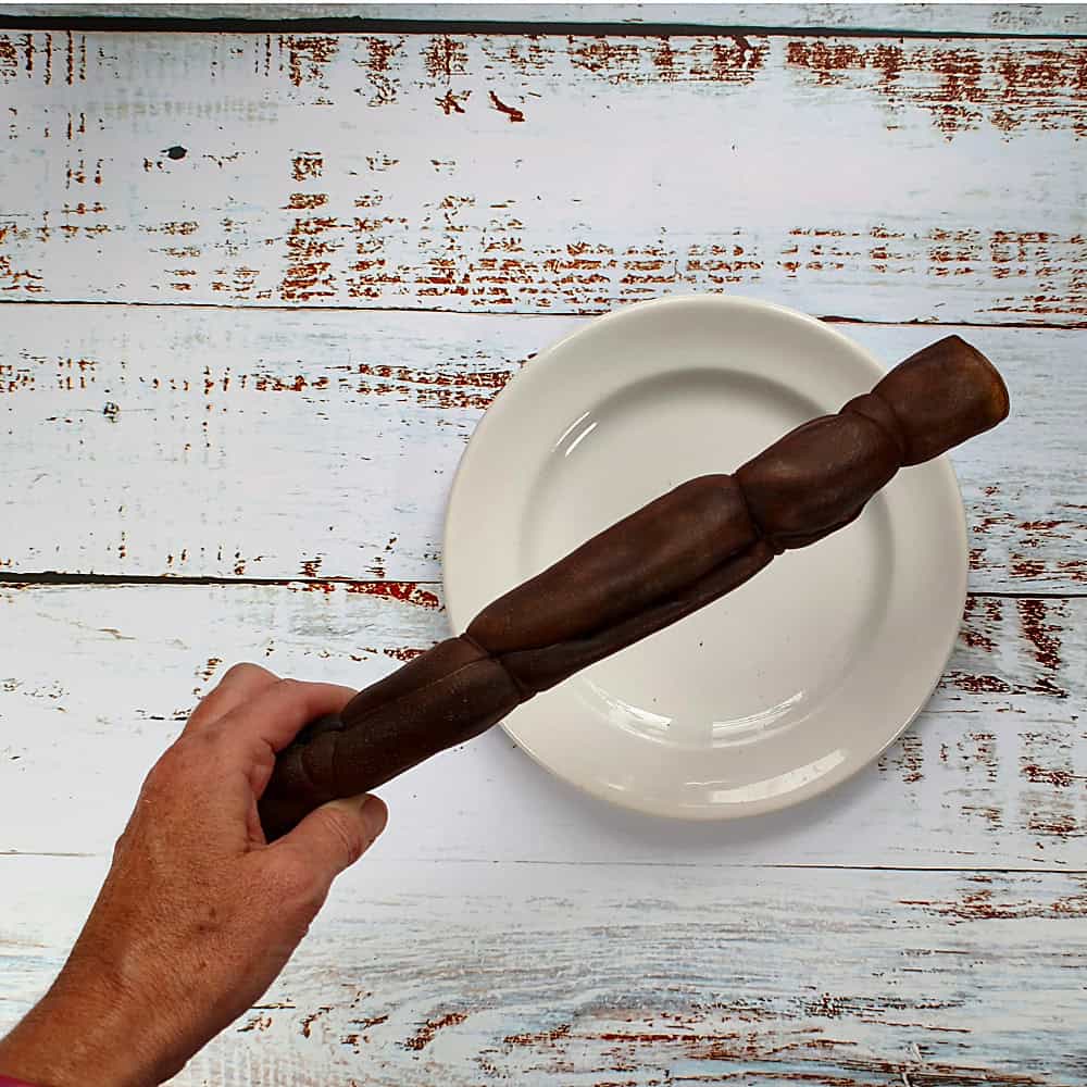 A medium camel roll dog chew held in a hand to show its size
