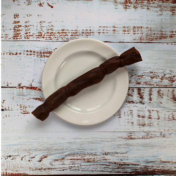 A medium camel roll dog chew on a cream plate on a whitewashed wooden board