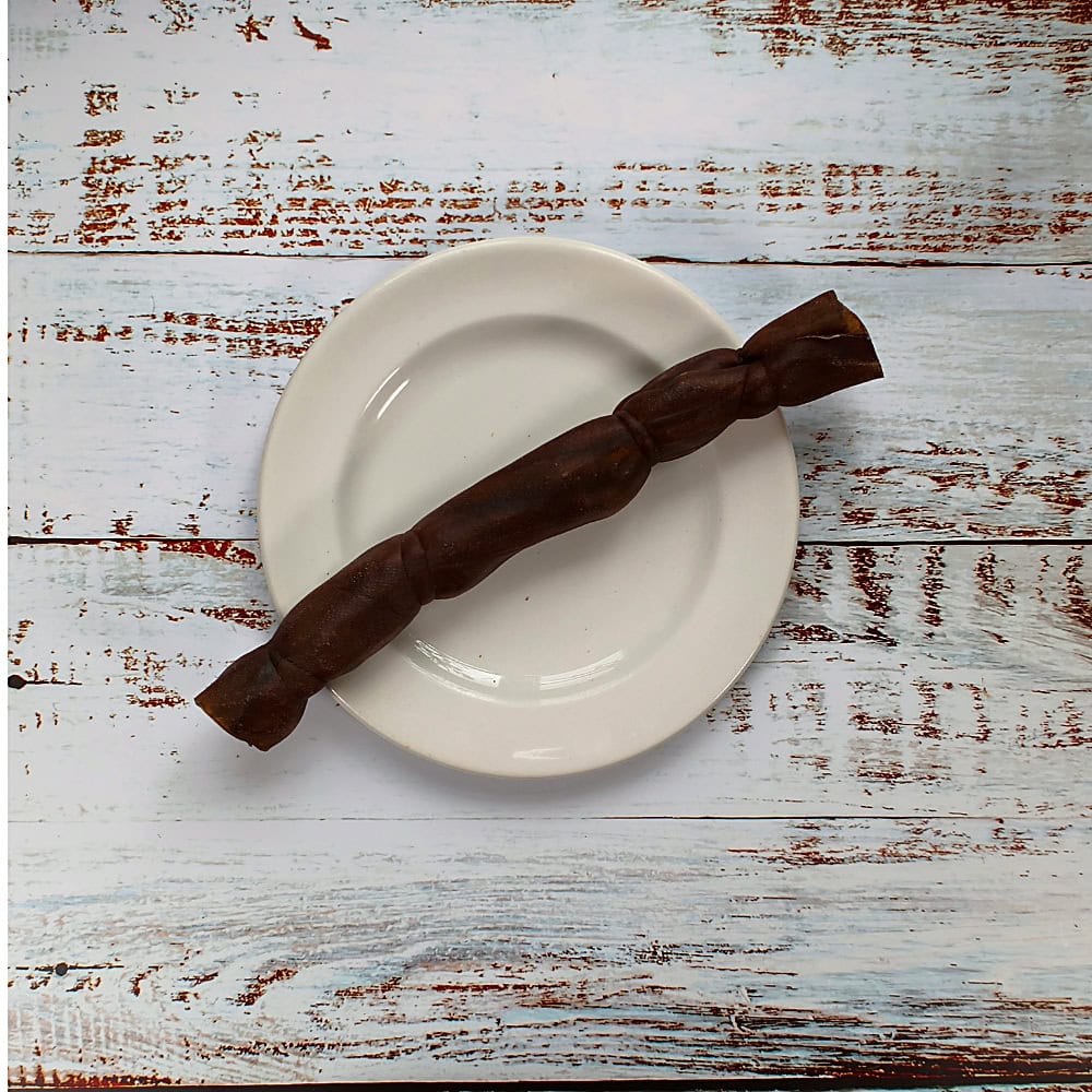 A medium camel roll dog chew on a cream plate on a whitewashed wooden board
