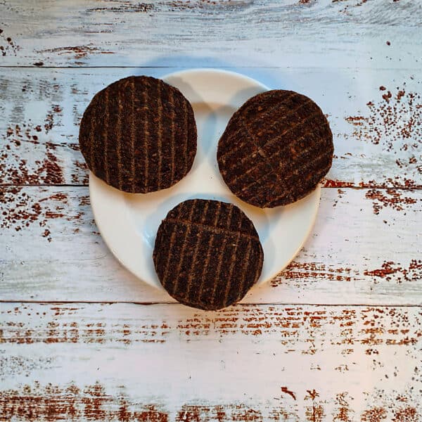 Three quarter pound beef burger dog treats on a cream plate showing their griddle lines
