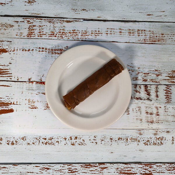 A single small camel roll dog chew on a cream plate on a whitewashed wooden board