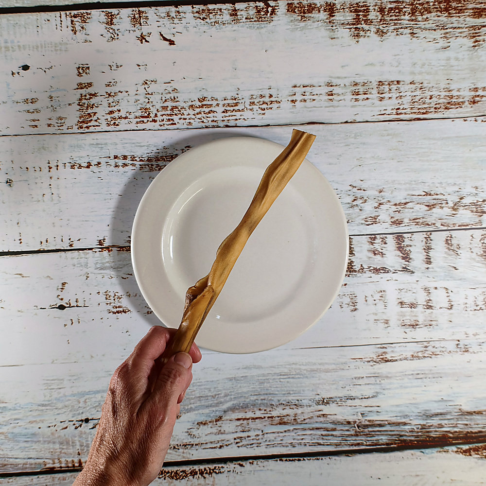 A single venison skin dog chew held in a hand to show its length