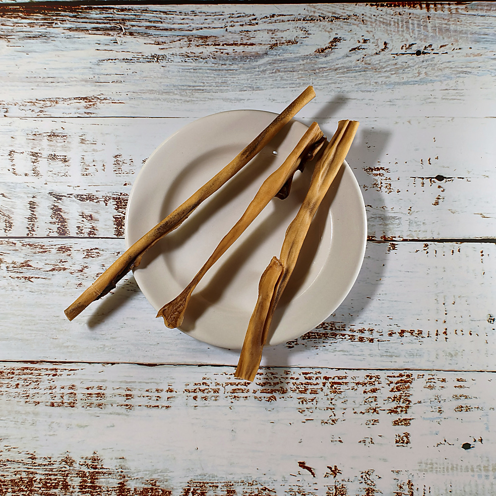 Three venison skin dog chews on a cream plate on a whitewashed wooden board