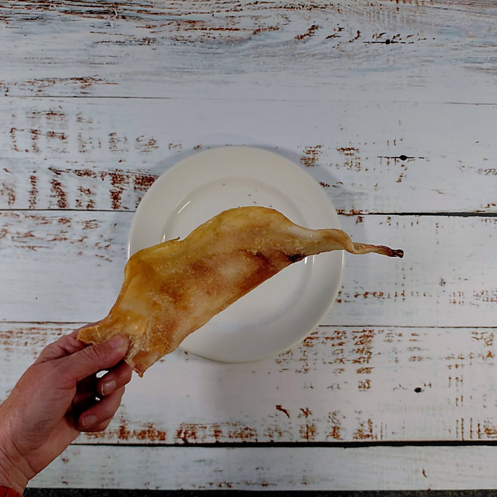 A moon bone natural dog chews held in a hand to give size on a whitewashed wooden board