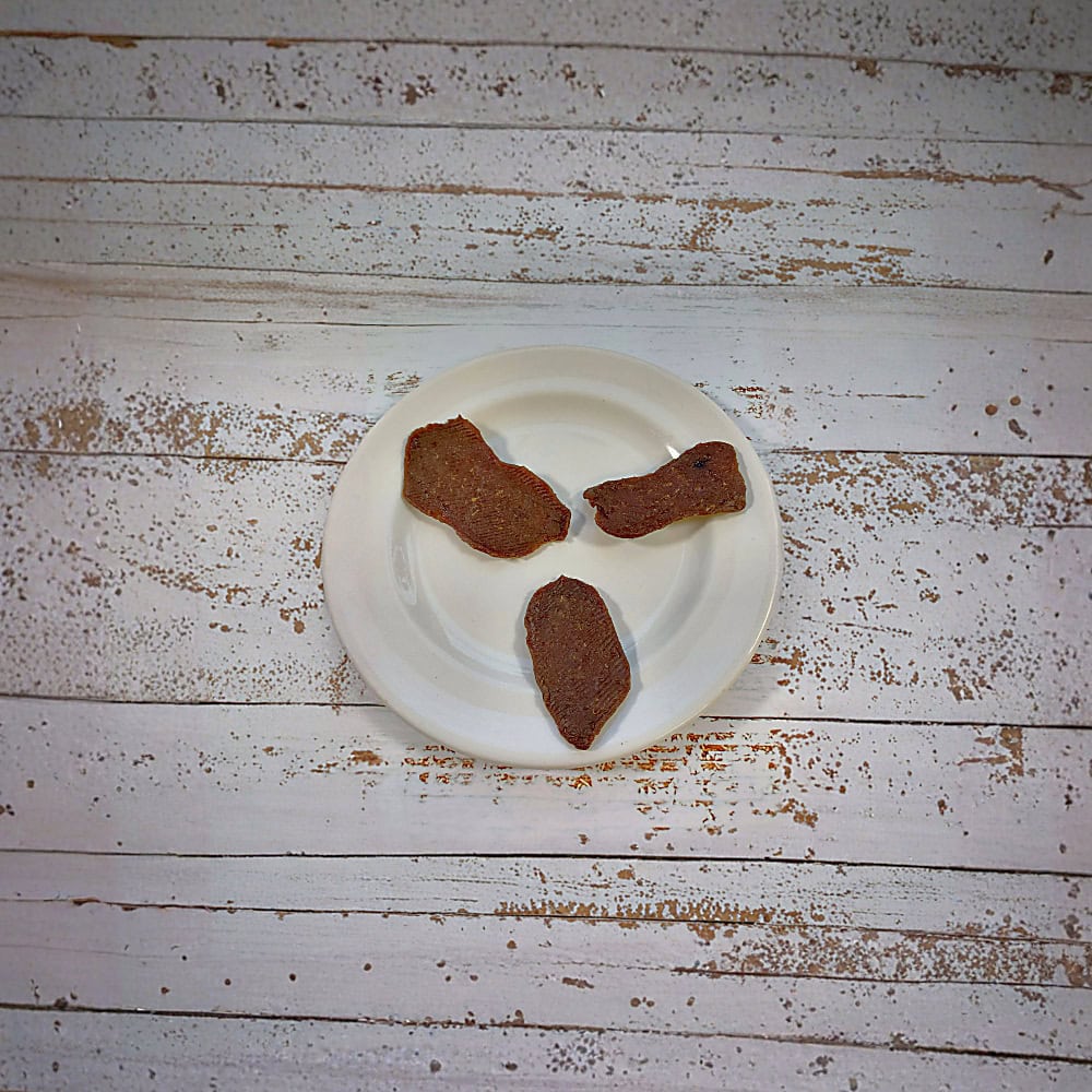 Three pieces of smoked ostrich natural dog treats on a cream plate on a whitewashed wooden board