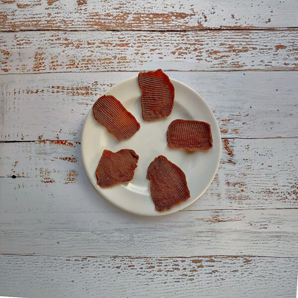 Five pieces of smoked ostrich natural dog treats on a cream plate on a whitewashed wooden board