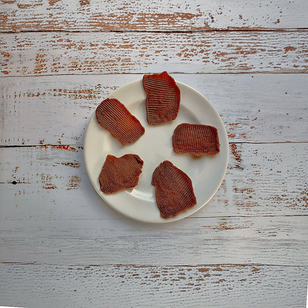 Five pieces of smoked ostrich natural dog treats on a cream plate on a whitewashed wooden board